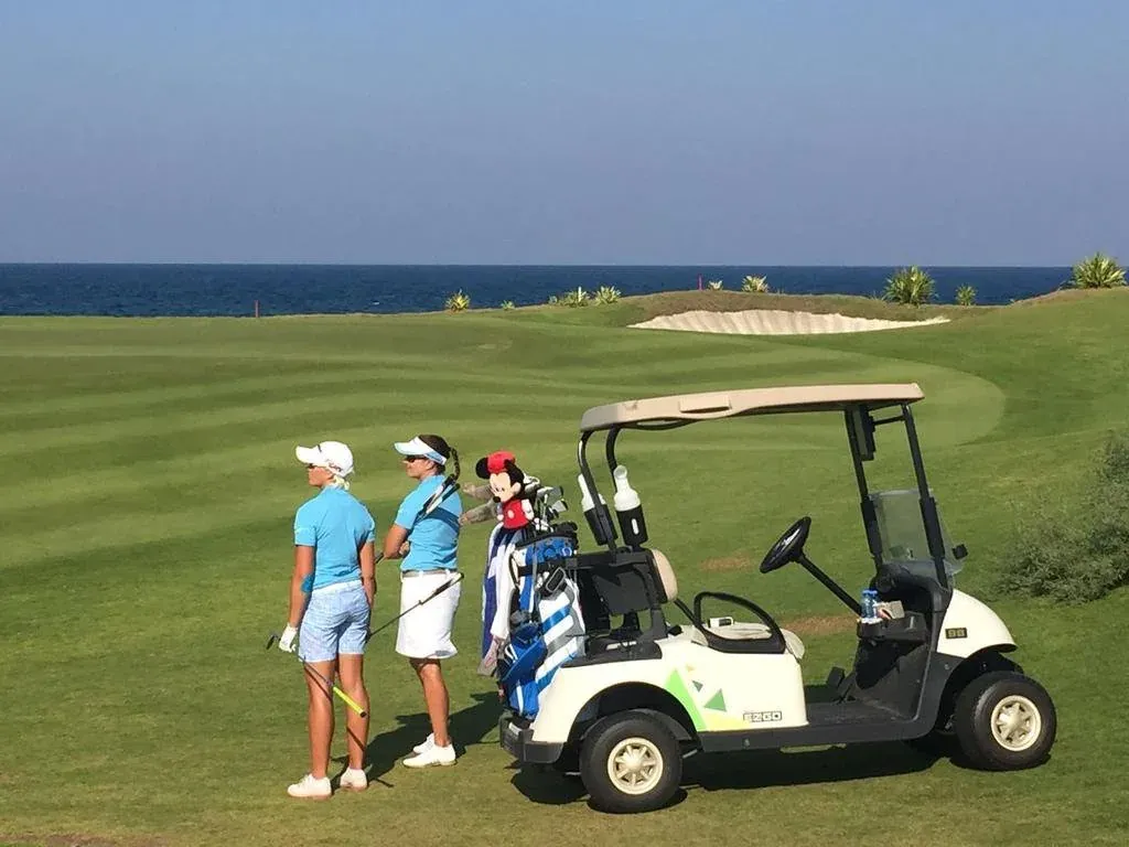 Golfers met een buggy bij een green langs de kustlijn van Al Mouj Golf in Muscat